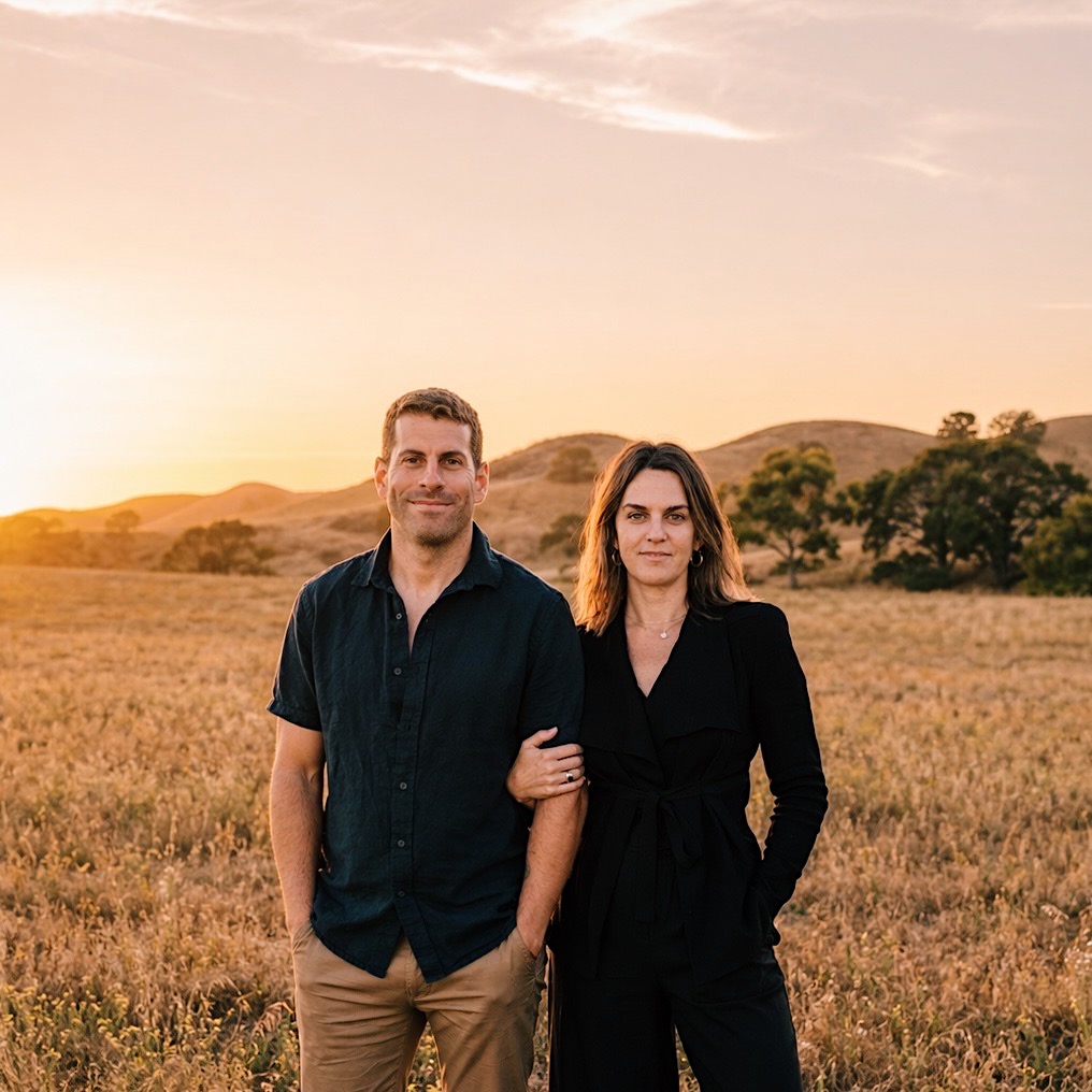 Zach and Samantha standing together in a field at sunset